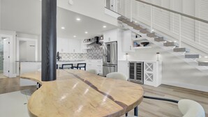 A spacious kitchen with modern appliances, a large wooden dining table, and a staircase leading to an upper level. - 516 Seascape | Oceanfront Condo with Pool Access in Wild Dunes (Isle Of Palms)