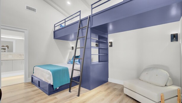 Una stanza con un letto a castello, una scala, un divano bianco e uno specchio.
