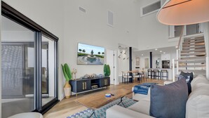 A modern living room with a sofa, coffee table, and TV. There's a staircase leading to an upper level. - 516 Seascape | Oceanfront Condo with Pool Access in Wild Dunes (Isle Of Palms)