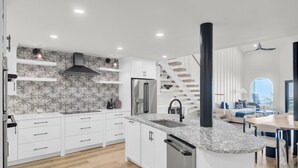 A modern kitchen with white cabinetry, a granite countertop, and a stainless steel refrigerator. - 516 Seascape | Oceanfront Condo with Pool Access in Wild Dunes (Isle Of Palms)