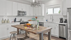 Una cocina moderna con armarios blancos, electrodomésticos de acero inoxidable, una isla de madera y una lámpara colgante.