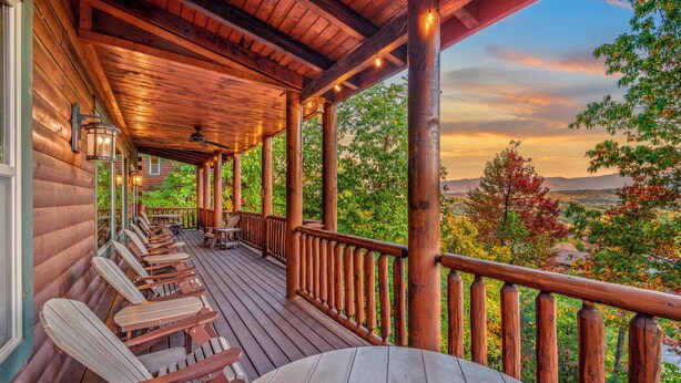 Una terraza de madera con sillas y una mesa, con vistas a un paisaje pintoresco de árboles y montañas.