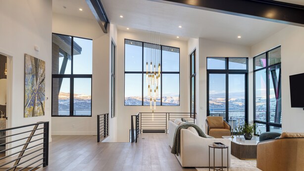 A spacious living area with large windows, a modern chandelier, and a view of the landscape.