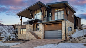 A modern multi-story house with a garage, large windows, and a balcony.