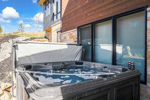 Un jacuzzi con tapa, un muro de piedra y un edificio de madera al fondo.