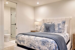 Un dormitorio con cama, mesita de noche, lámpara y baño con inodoro y ducha.