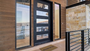 A modern building entrance with a black door, glass panels, and a stone wall.