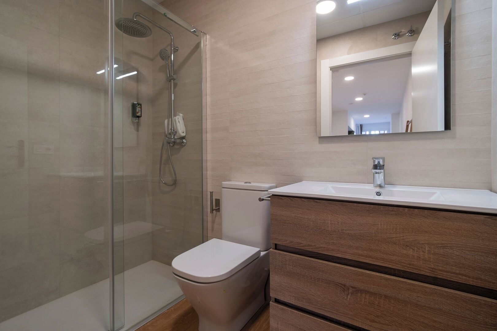 Een moderne badkamer met een douchecabine van glas, een wit toilet en een houten wastafelmeubel met spiegel.