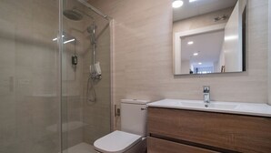 Ein modernes Badezimmer mit einer Duschkabine aus Glas, einer weißen Toilette und einem hölzernen Waschtisch mit Spiegel.