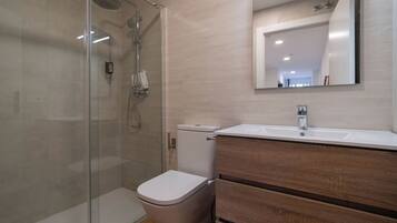 Een moderne badkamer met een douchecabine van glas, een wit toilet en een houten wastafelmeubel met spiegel.