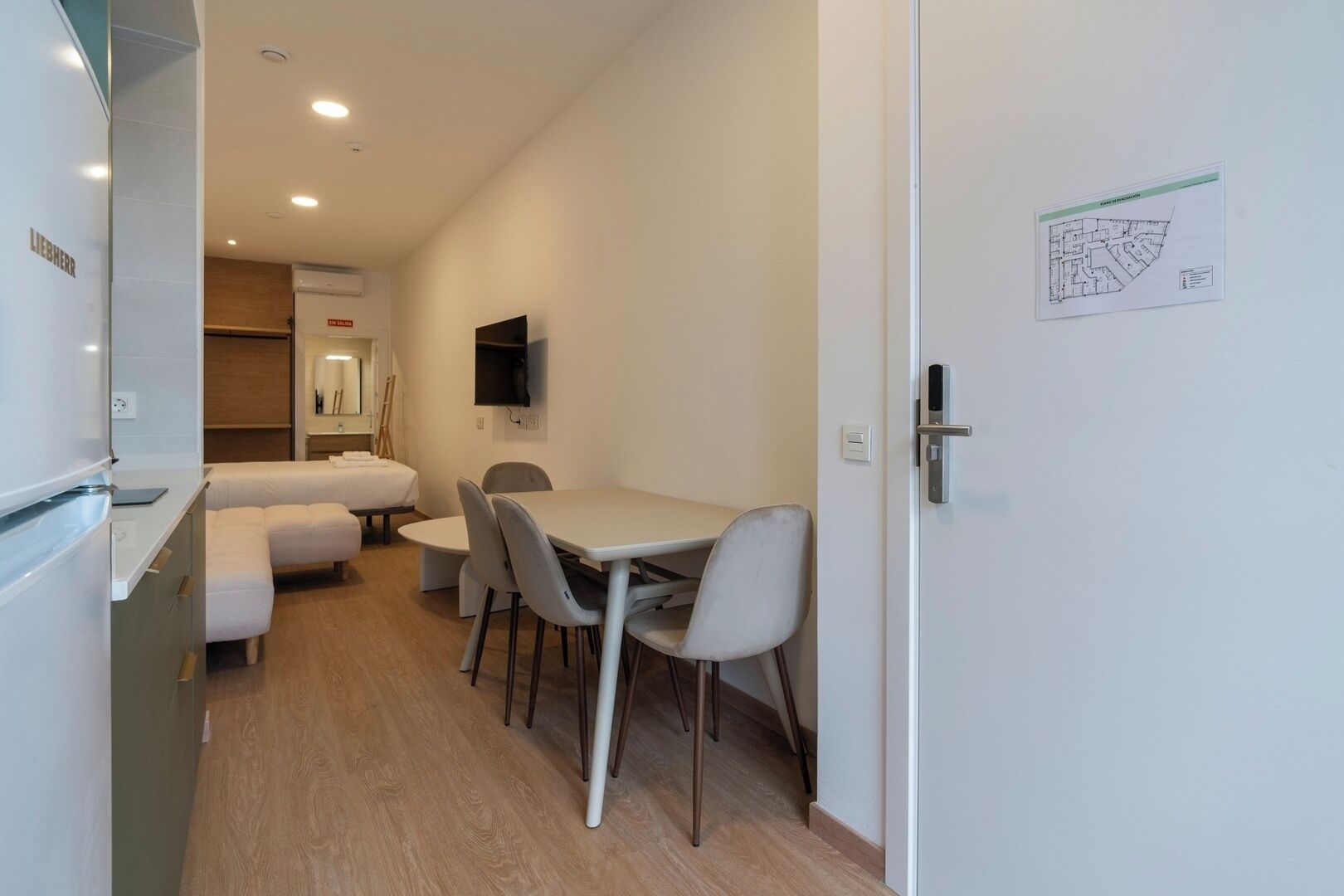 Een compacte hotelkamer met een kitchenette, een bed, een kleine eettafel met stoelen en een flatscreen televisie aan de muur.