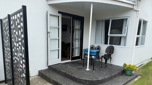 Ein weißes Gebäude mit einem geschwungenen Eingang, einem schwarzen Metallgitter, einer Treppe, die zu einer Veranda führt, und zwei Stühlen auf der Veranda.