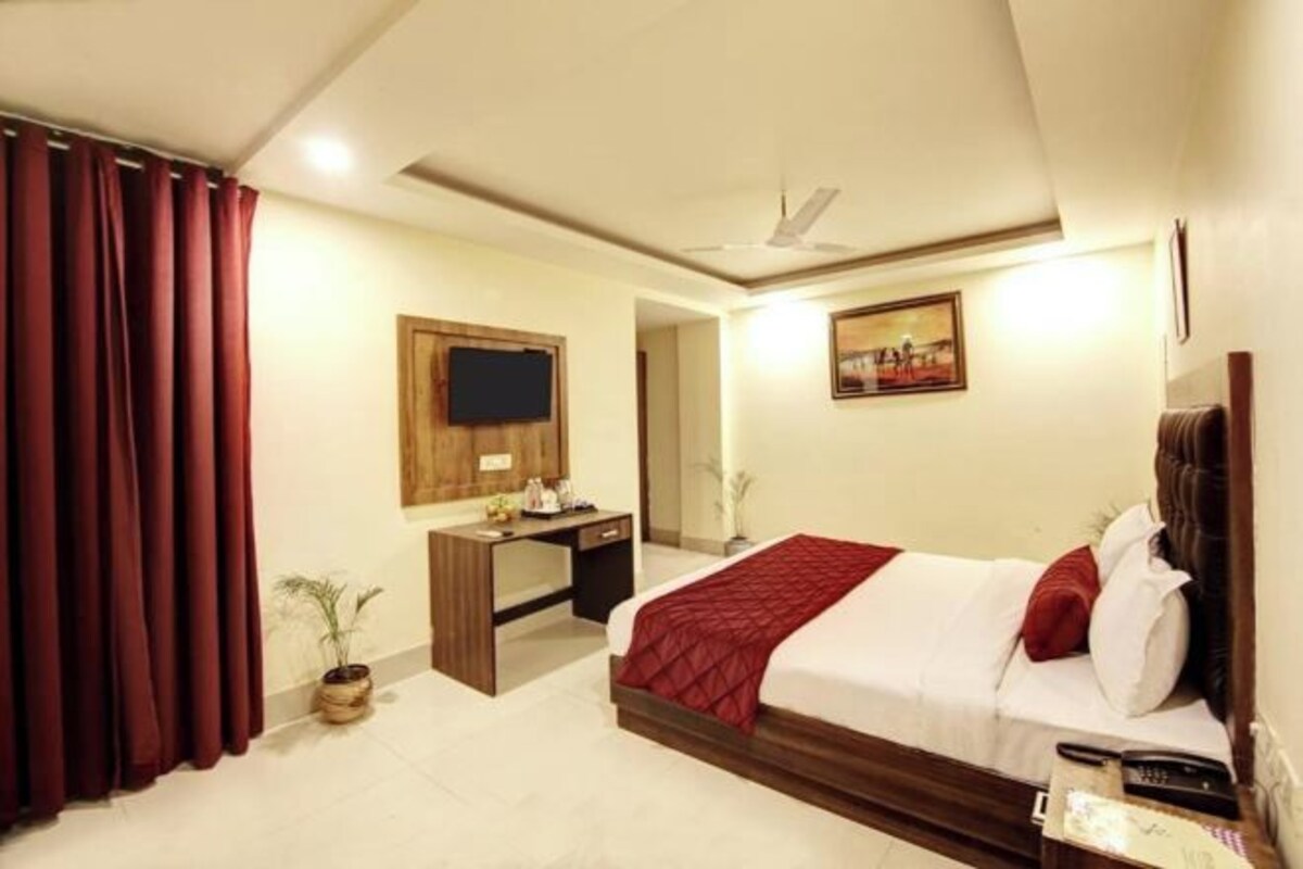 A hotel room with a bed, a desk, a television, and a painting on the wall.