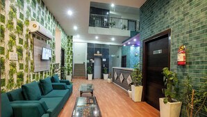 A lobby with green sofas, a glass coffee table, potted plants, and a fire extinguisher. - Hotel Sky View (New Delhi)