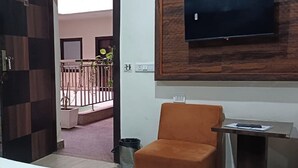 A hotel room with a bed, an orange armchair, a small table with a remote control, and a TV mounted on the wall. - Hotel Sky View (New Delhi)