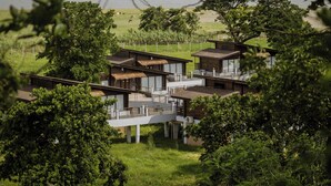 A modern resort with multiple buildings connected by walkways, surrounded by lush greenery and a body of water in the background. - Rhino and River Wildlife Retreat & Spa, Pobitora - Small Luxury Hotels of the World (Mangaldai)