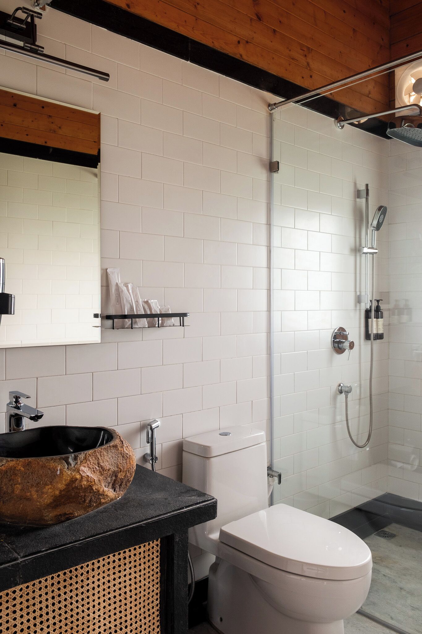 A modern bathroom with a stone sink, white toilet, and a glass-enclosed shower area.