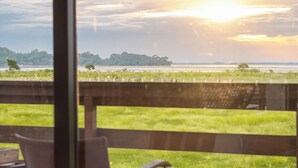 A balcony with two chairs and a table, overlooking a grassy field and a distant horizon. - Rhino and River Wildlife Retreat & Spa, Pobitora - Small Luxury Hotels of the World (Mangaldai)