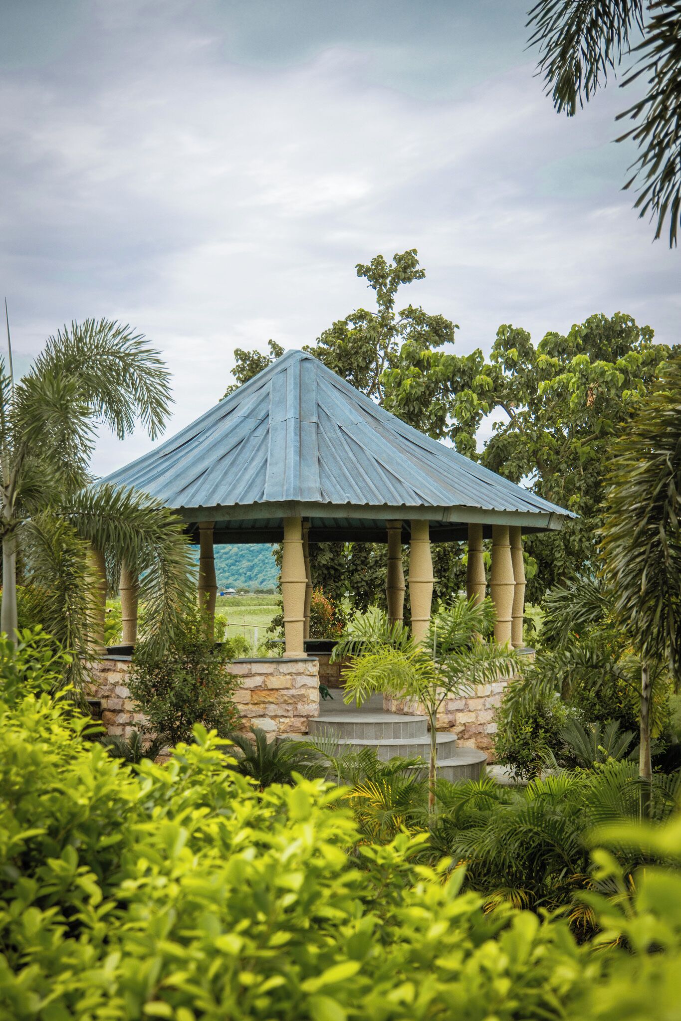 A gazebo with a blue roof, surrounded by lush greenery and stone walls.