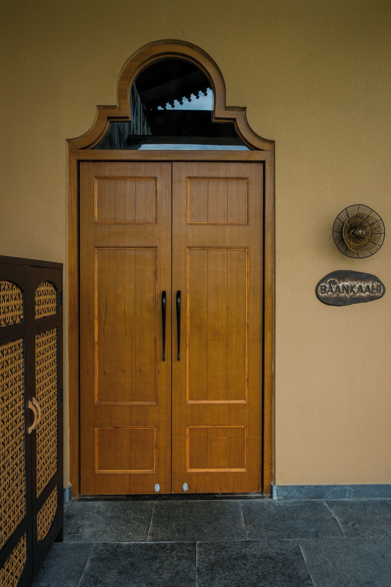 A wooden double door with a decorative arch above it, a metal sign on the wall, and a tiled floor.