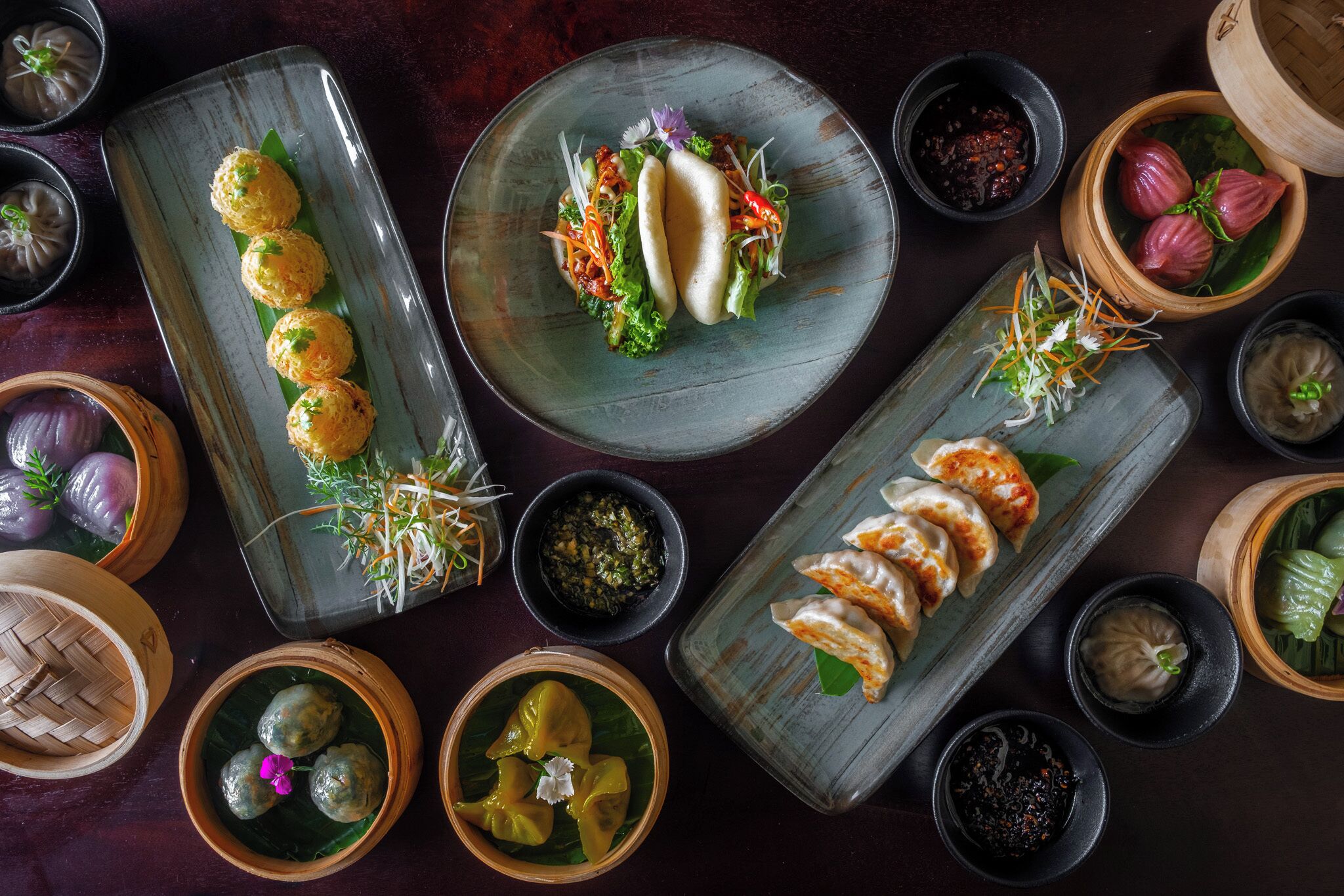 Variedad de platos asiáticos, como dumplings y rollitos primavera, presentados en una mesa con recipientes pequeños de salsas y guarniciones.