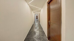 Um corredor com porta de madeira à direita, piso de mármore e iluminação embutida no teto.