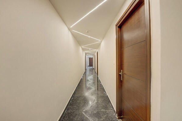 A hallway with a wooden door on the right, a marble floor, and recessed lighting along the ceiling.