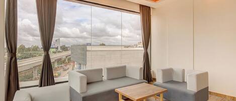 A modern living room with a grey sofa, a wooden coffee table, and large windows with curtains.