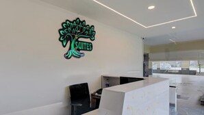 Uma área de recepção com design moderno, destacando uma grande placa iluminada com a palavra "SUITES" e um balcão de atendimento.