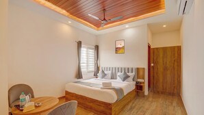 Quarto de hotel com teto de madeira, cama com cabeceira, mesa de cabeceira, cadeira, pequena mesa com uma garrafa e um telefone, e uma porta.
