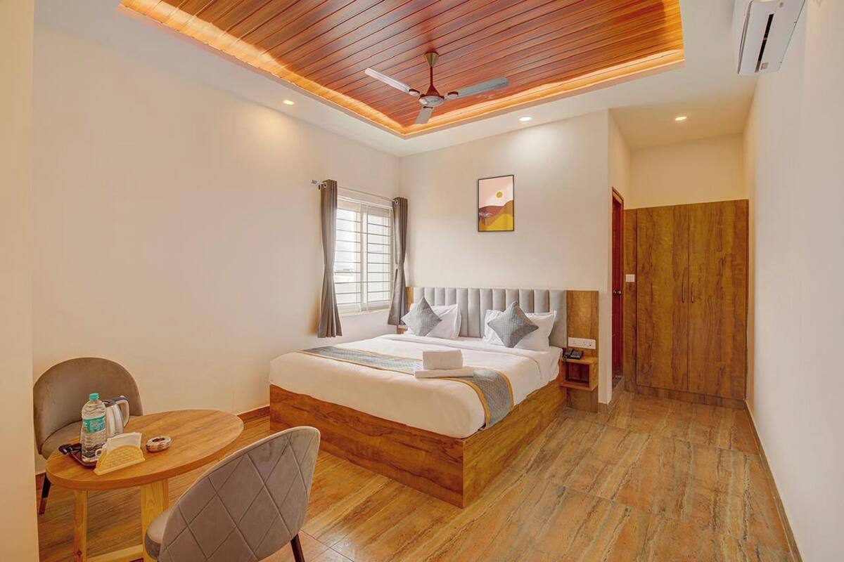 A hotel room with a wooden ceiling, a bed with a headboard, a bedside table, a chair, a small table with a bottle and a phone, and a door.