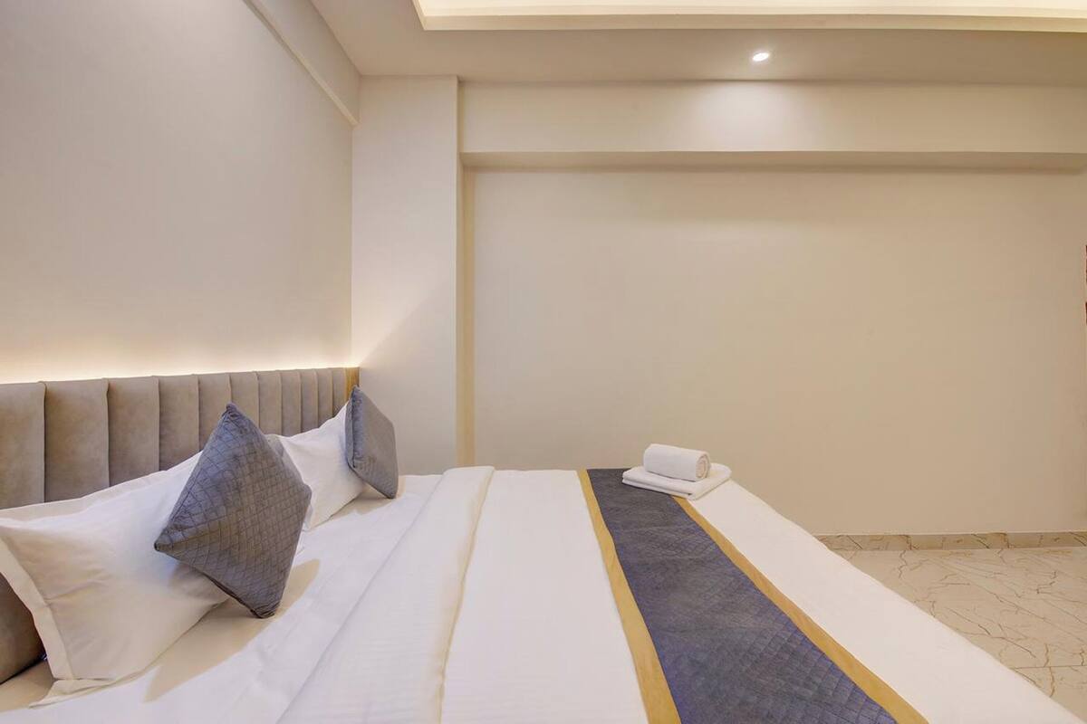 A hotel room with a large bed, a headboard, and a small table with a rolled towel.