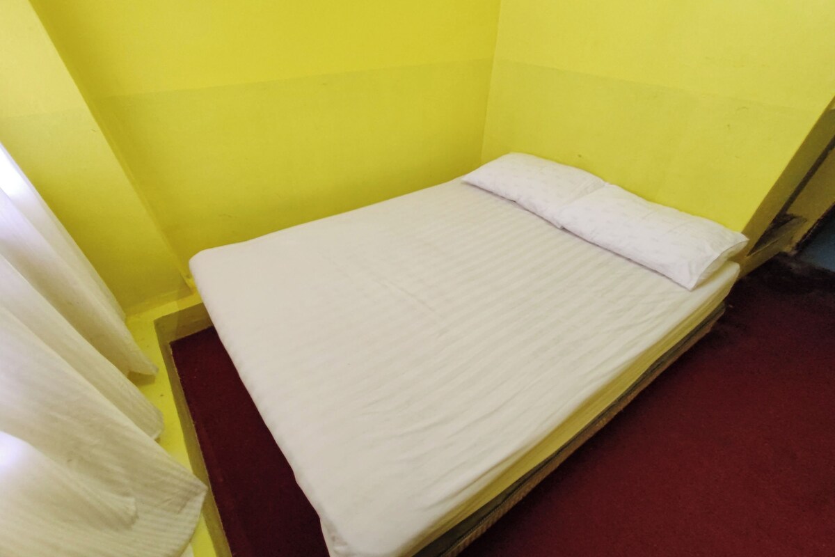 A single bed with a white mattress and pillow in a room with yellow walls and a red carpet.