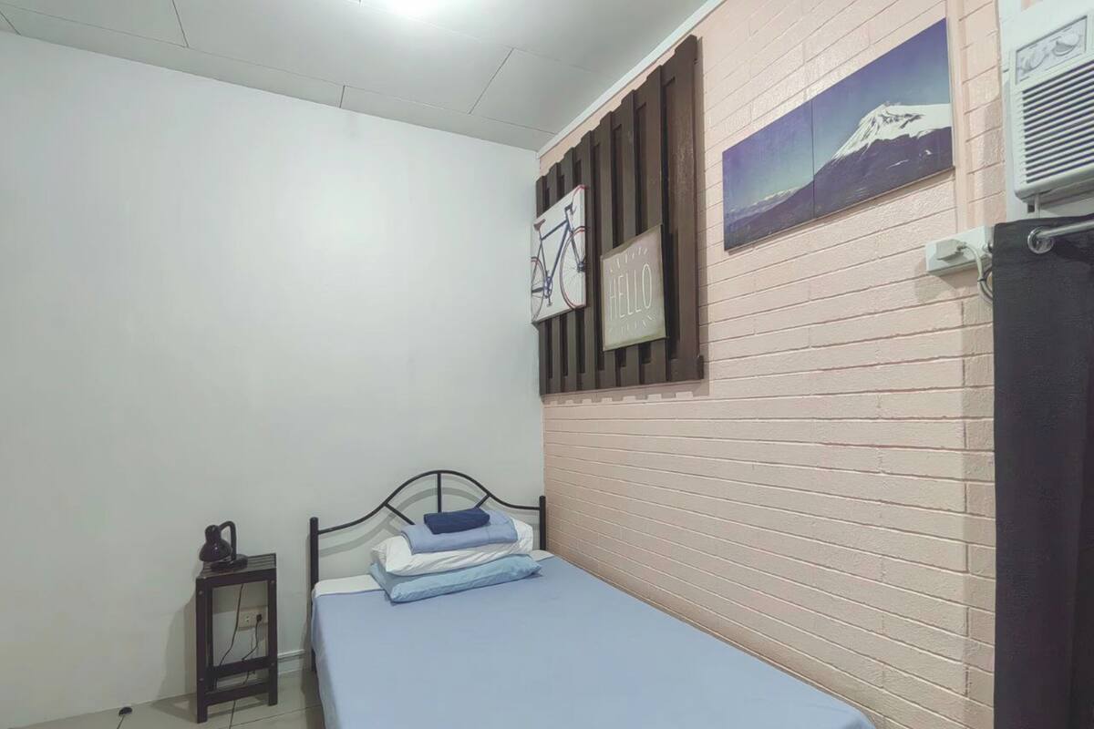 Una camera da letto con un letto, un tavolino con una lampada, un condizionatore d'aria a muro e un quadro appeso raffigurante una montagna.