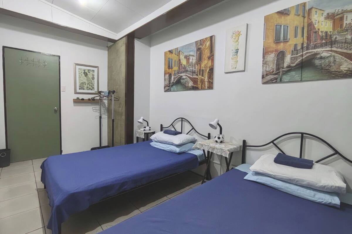 Una camera d'albergo con due letti, una scrivania, una sedia, una lampada e opere d'arte alle pareti.