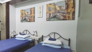 Een kamer met twee bedden, elk voorzien van een blauw sprei en kussens, en een kleine tafel met een lamp en een decoratief object.