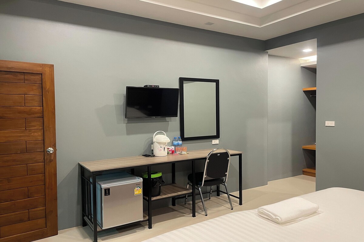 A bedroom with a bed, a desk with a chair, a television, and a mirror.