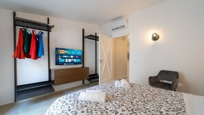 Une chambre d’hôtel équipée d’un lit, d’une télévision, d’une armoire, d’une chaise et d’une porte donnant sur une autre pièce.