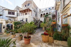 A courtyard with potted plants, a tree, and buildings with balconies and arches. - Elegant flat of 41 sqm, for up to four people, located on the first floor (NO elevator). The property is located in the heart of Ortigia, in a Restricted-Traffic Area, within the historic Cortile Abela (Abela courtyard), 350 mt from the market and only 2 (Siracusa)