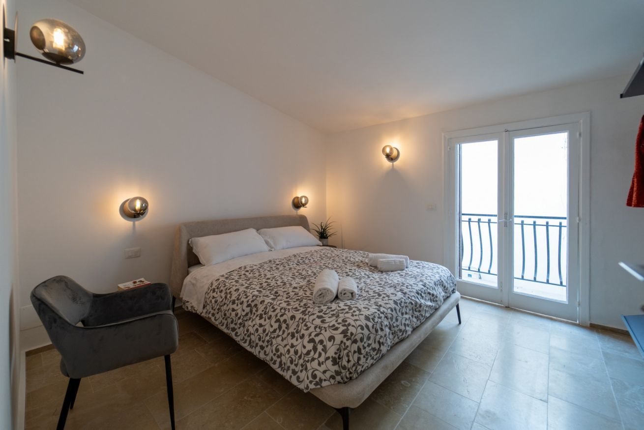 A bedroom with a bed, bedside lamps, a chair, and a balcony.