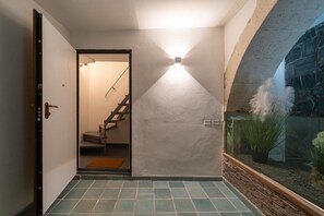 A hallway with a staircase, a light fixture, and a glass enclosure with plants. - Elegant flat of 41 sqm, for up to four people, located on the first floor (NO elevator). The property is located in the heart of Ortigia, in a Restricted-Traffic Area, within the historic Cortile Abela (Abela courtyard), 350 mt from the market and only 2 (Siracusa)