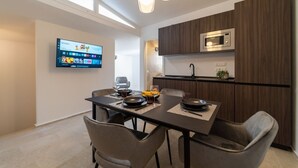 Une cuisine moderne équipée d’un téléviseur à écran plat, de meubles en bois, d’un four à micro-ondes et d’un coin repas avec des chaises et une table dressée pour deux personnes.