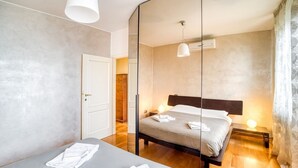 Ein modernes Hotelzimmer mit einem großen Spiegel, einem Bett mit ordentlich gefalteten Handtüchern, einer Nachttischlampe und Holzboden.