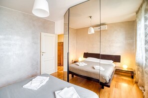 A modern hotel room with a large mirror, a bed with neatly folded towels, a bedside lamp, and a wooden floor. - GuestHost - Cosy flat of 80 sqm, sleeping 4 people, on the 2nd floor of a building (NO lift and stairs to access) with covered PARKING SPACE and shared garden with gazebo.We are located in San Martino in Campo, a hamlet of Perugia, which enjoys a strateg (San Martino in Campo)
