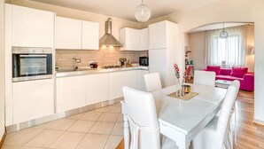 Eine moderne Küche mit weißen Schränken, ein Essbereich mit Tisch und Stühlen sowie ein Wohnzimmer mit einem rosa Sofa.