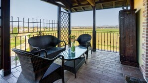 Eine überdachte Terrasse mit Korbmöbeln und einem Glastisch, mit Blick auf ein eingezäuntes Feld.