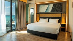 A modern hotel room with a large bed, a ceiling fan, a large window with curtains, a view of the ocean, and a wall-mounted artwork. - Athiri Residence Dhiffushi (Dhiffushi)