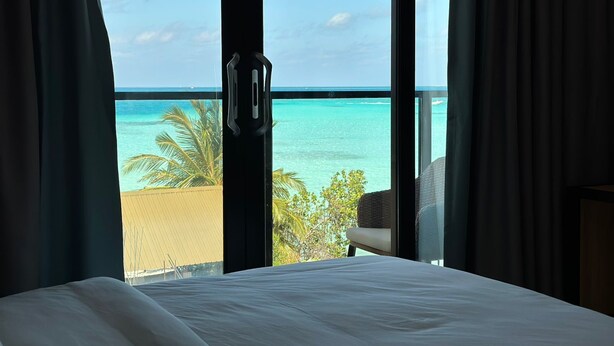 A hotel room with a large window offering a view of the ocean and palm trees. - Athiri Residence Dhiffushi (Dhiffushi)