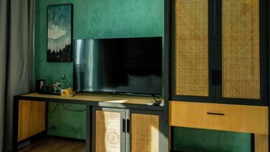 A room with a large flat-screen TV mounted on a wall, a wooden desk with a lamp, and a green accent wall. - Athiri Residence Dhiffushi (Dhiffushi)