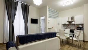 A modern living room with a sofa, a dining table with chairs, a kitchen area with cabinets and appliances, and a TV mounted on the wall. - GuestHost - La Spezia Mon Amour - Pet Friendly (La Spezia)